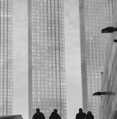 Silhouetted pedestrians in an urban landscape by skyscrapers in black and white.
